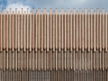 Eine Besonderheit der vorgehängten Holzfassade besteht in der Staffelung der einzelnen Kantholzebenen nach oben und außen. Die Mehrzweckhalle staffelt sich in zwei, die Dreifeldhalle in drei Ebenen. Die Kronen erhalten ihren Abschluss durch kleine Kupferkäppchen, die das Stirnholz auf seinen variierenden Höhen schützt. | © Marcus Ebener